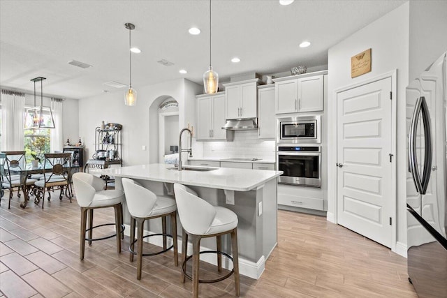 17936 Adrift Rd, Winter Garden, FL 34787 - kitchen with stainless steel appliances, a sink, under cabinet range hood, backsplash, and light wood-style flooring