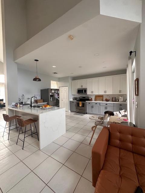9202 Olmstead Dr, Lake Worth, FL 33467 - kitchen with appliances with stainless steel finishes, a peninsula, light tile patterned flooring, a breakfast bar area, and white cabinetry