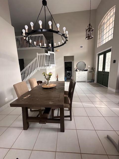 9202 Olmstead Dr, Lake Worth, FL 33467 - dining room featuring a chandelier, a towering ceiling, light tile patterned floors, stairway, and baseboards