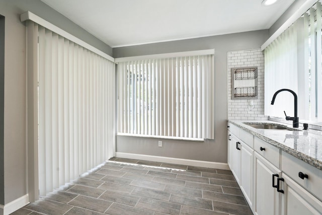 2307 SE Seafury Ln SE, Port Saint Lucie, FL 34952 - kitchen featuring a sink, light stone counters, baseboards, and white cabinetry