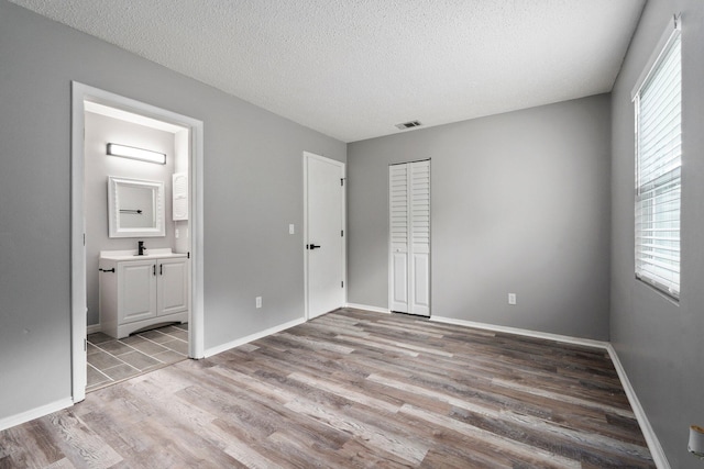 2307 SE Seafury Ln SE, Port Saint Lucie, FL 34952 - unfurnished bedroom with light wood finished floors, a textured ceiling, connected bathroom, baseboards, and a closet