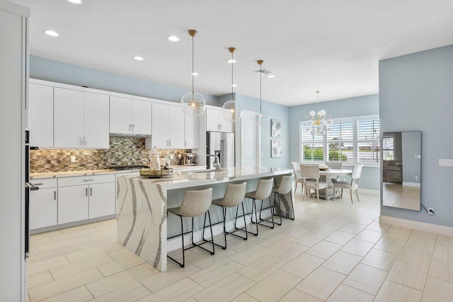 983 Hookline Cir, The Acreage, FL 33470 - kitchen featuring stainless steel appliances, backsplash, a sink, a kitchen breakfast bar, and white cabinetry
