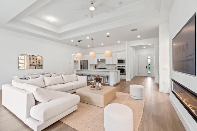 10803 Stellar Cir, Palm Beach Gardens, FL 33412 - living room featuring a tray ceiling, ornamental molding, a ceiling fan, recessed lighting, and light wood-type flooring