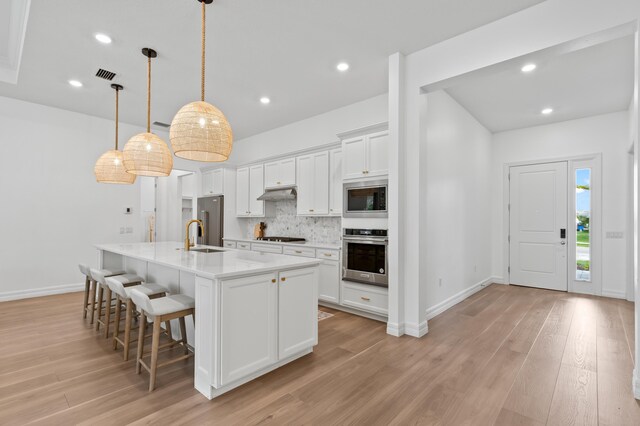 10803 Stellar Cir, Palm Beach Gardens, FL 33412 - kitchen featuring stainless steel appliances, under cabinet range hood, a kitchen breakfast bar, backsplash, and white cabinetry