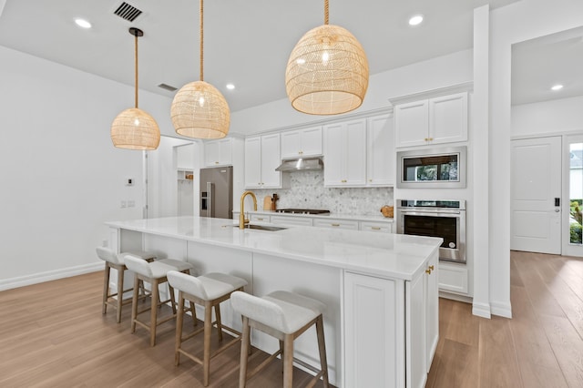 10803 Stellar Cir, Palm Beach Gardens, FL 33412 - kitchen featuring stainless steel appliances, a sink, backsplash, light wood-style floors, and white cabinets