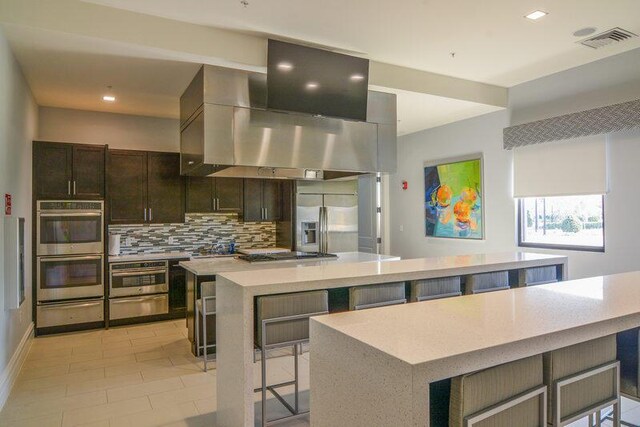 24038 SW Firenze Way, Port Saint Lucie, FL 34986 - kitchen with appliances with stainless steel finishes, a large island, a warming drawer, backsplash, and a breakfast bar