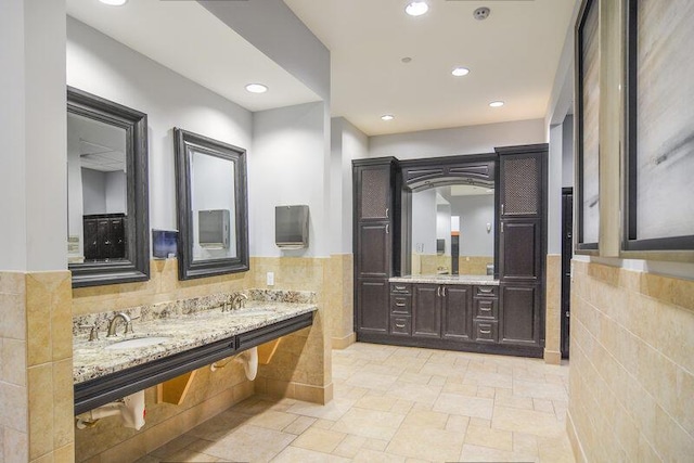 24038 SW Firenze Way, Port Saint Lucie, FL 34986 - full bathroom featuring tile walls, double vanity, a wainscoted wall, recessed lighting, and stone tile floors