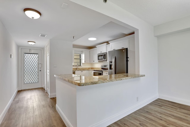 2430 Deer Creek Country Club Blvd Unit 205-2, Deerfield Beach, FL 33442 - kitchen featuring appliances with stainless steel finishes, light wood finished floors, white cabinets, a peninsula, and light stone counters
