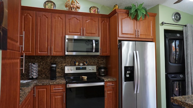 804 Sky Pine Way Unit C, Greenacres, FL 33415 - kitchen with stainless steel appliances, stacked washing machine and dryer, decorative backsplash, dark stone countertops, and brown cabinets