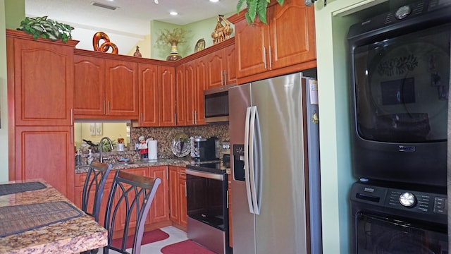 804 Sky Pine Way Unit C, Greenacres, FL 33415 - kitchen featuring appliances with stainless steel finishes, estacked washer and dryer, backsplash, a sink, and brown cabinetry