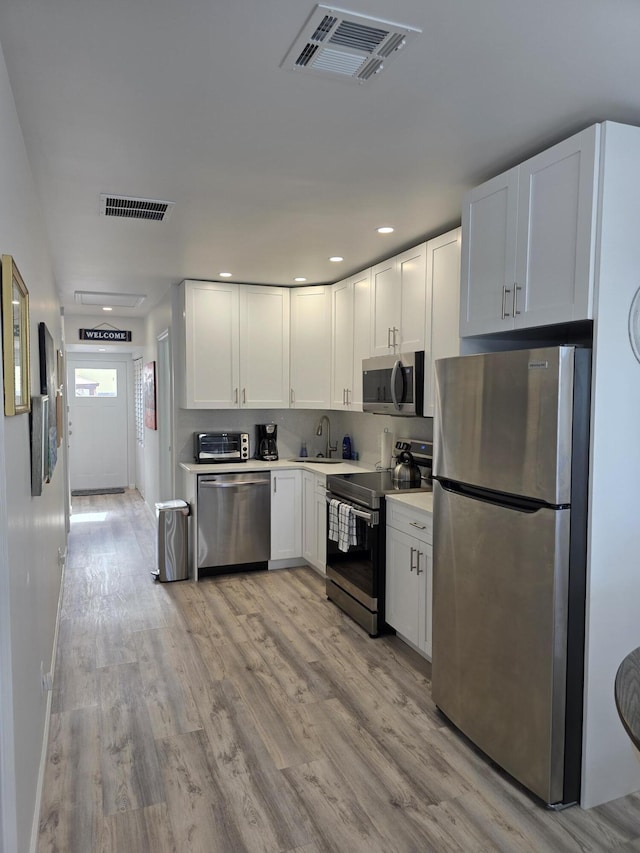 319 N J St, Lake Worth Beach, FL 33460 - kitchen with stainless steel appliances, white cabinetry, light countertops, light wood-style flooring, and a sink