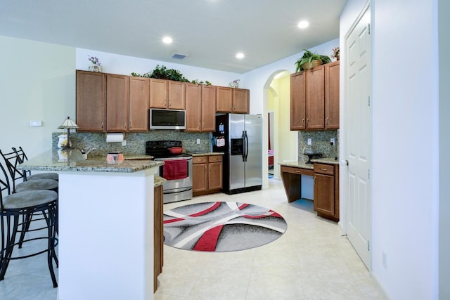 17560 72nd Rd N, The Acreage, FL 33470 - kitchen with appliances with stainless steel finishes, tasteful backsplash, a kitchen bar, a peninsula, and arched walkways