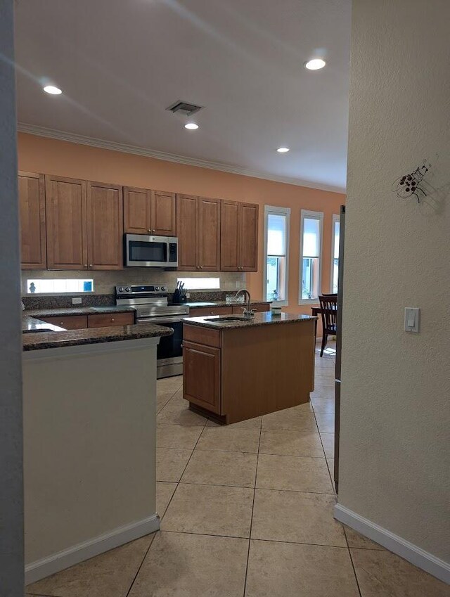 3104 SW Porpoise Cir, Stuart, FL 34997 - kitchen with stainless steel appliances, a sink, an island with sink, ornamental molding, and dark stone countertops