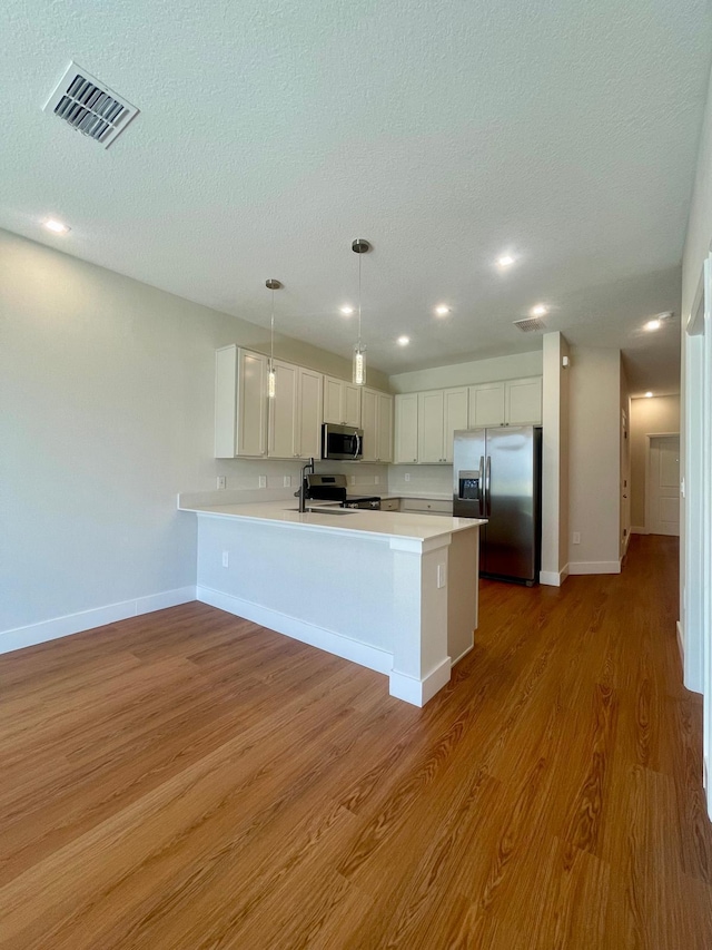 6159 Peaceful Park Way, Clermont, FL 34714 - kitchen featuring appliances with stainless steel finishes, a peninsula, light countertops, wood finished floors, and white cabinets