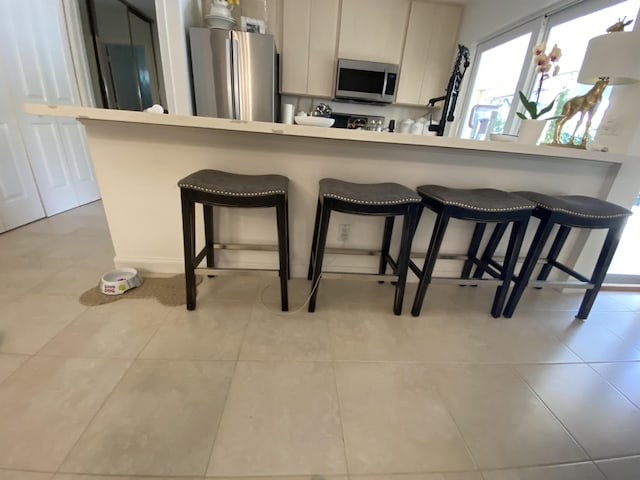 9124 Sun Terrace Cir Unit D, West Palm Beach, FL 33403 - kitchen with stainless steel appliances, a breakfast bar area, light tile patterned floors, and light countertops