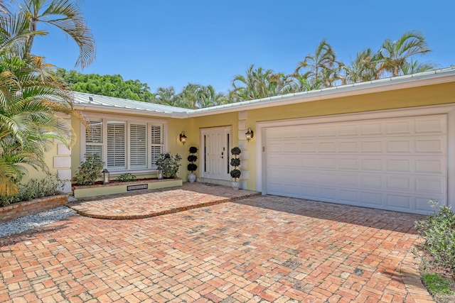 134 Worth Ct N, West Palm Beach, FL 33405 - view of front facade featuring decorative driveway, stucco siding, metal roof, and a garage