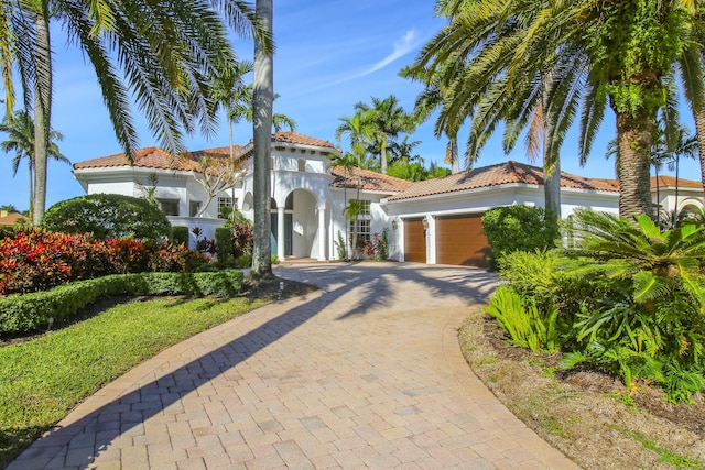 1186 Breakers W Blvd, West Palm Beach, FL 33411 - mediterranean / spanish-style home featuring an attached garage, a tiled roof, decorative driveway, and stucco siding