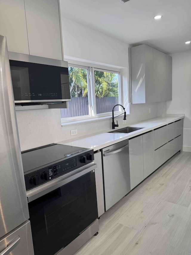 3056 NE 14th Ave, Oakland Park, FL 33334 - kitchen with appliances with stainless steel finishes, a sink, modern cabinets, light countertops, and light wood finished floors