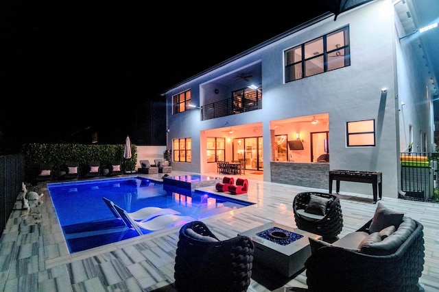 8305 Fishhawk Falls Ct, Boca Raton, FL 33496 - back of house at night featuring a balcony, stucco siding, an outdoor living space with a fire pit, and stone siding