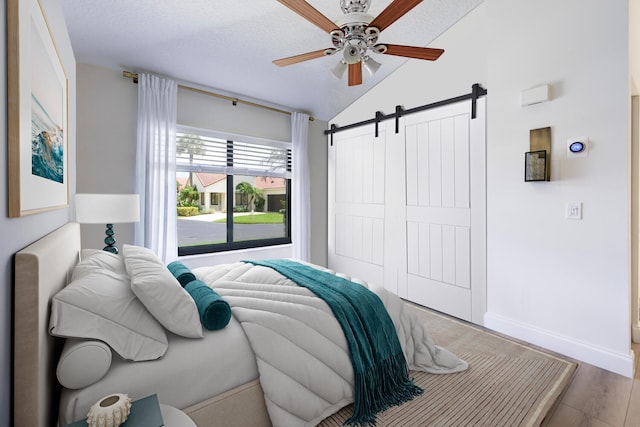 508 Sea Oats Dr Unit A-1, Juno Beach, FL 33408 - bedroom with a barn door, lofted ceiling, a textured ceiling, wood finished floors, and baseboards