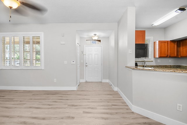 1595 SE Pomeroy St, Stuart, FL 34997 - kitchen with brown cabinets, light wood finished floors, baseboards, a ceiling fan, and dark stone countertops