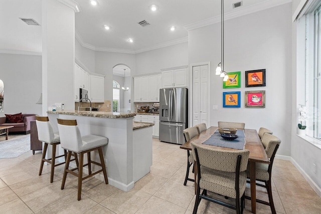 102 Andalusia Way, Palm Beach Gardens, FL 33418 - kitchen featuring stainless steel fridge, ornamental molding, a peninsula, white cabinets, and a kitchen bar