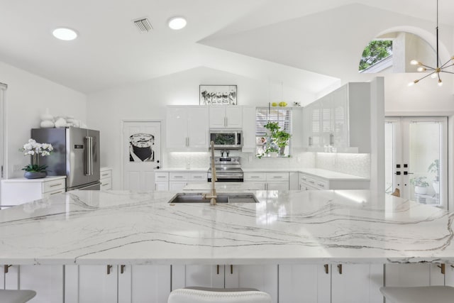 13853 Palm Grove Pl, West Palm Beach, FL 33418 - kitchen featuring appliances with stainless steel finishes, lofted ceiling, a kitchen bar, white cabinets, and light stone counters