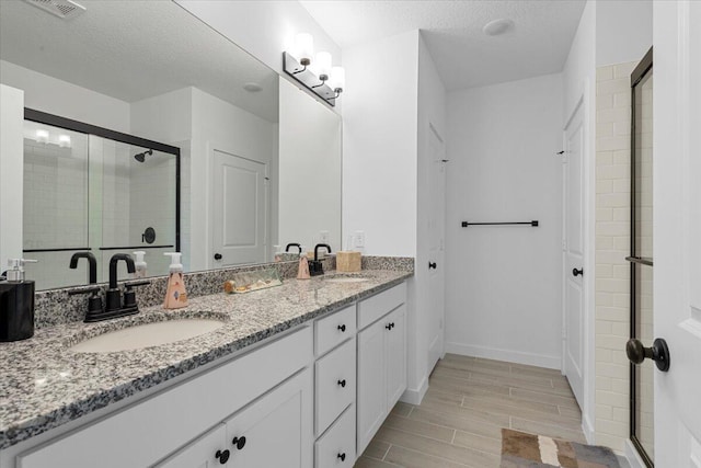 821 NE Trailside Run, Port Saint Lucie, FL 34983 - bathroom with double vanity, a stall shower, wood tiled floors, a textured ceiling, and baseboards
