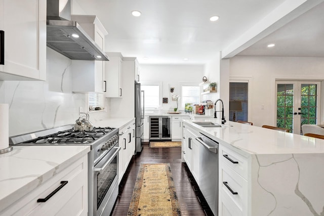 806 Sunset Rd, West Palm Beach, FL 33401 - kitchen featuring wall chimney exhaust hood, stainless steel appliances, wine cooler, recessed lighting, and light stone counters