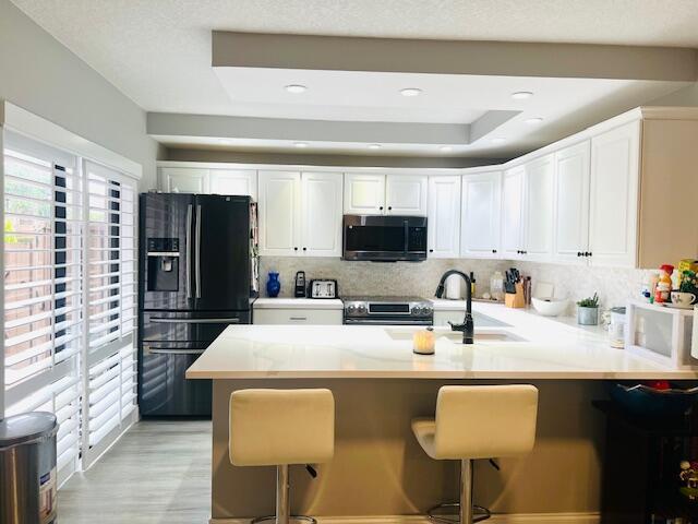 1714 17th Ct, Jupiter, FL 33477 - kitchen with appliances with stainless steel finishes, a peninsula, tasteful backsplash, white cabinets, and a kitchen breakfast bar
