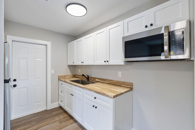 617 54th St, West Palm Beach, FL 33407 - kitchen with stainless steel microwave, a sink, wood finished floors, wood counters, and white cabinets