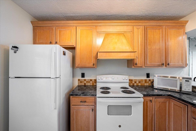 1950 SW Palm City Rd Unit 5109, Stuart, FL 34994 - kitchen with white appliances, premium range hood, a textured ceiling, brown cabinetry, and dark stone countertops