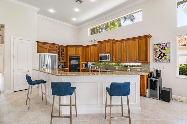 16414 Braeburn Ridge Trl, Delray Beach, FL 33446 - kitchen featuring appliances with stainless steel finishes, a high ceiling, brown cabinetry, beverage cooler, and ornamental molding