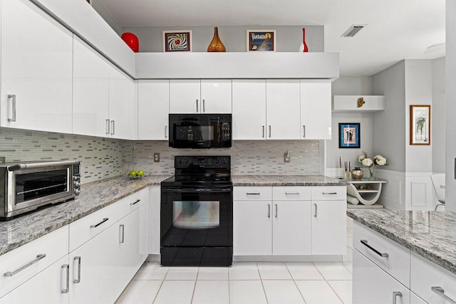 137 N Lakeshore Dr, Hypoluxo, FL 33462 - kitchen with black appliances, white cabinetry, a wainscoted wall, light stone counters, and light tile patterned flooring