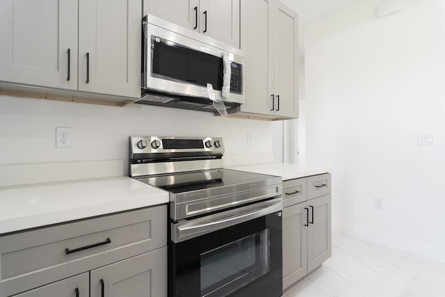 4209 25th St SW, Lehigh Acres, FL 33976 - kitchen with stainless steel appliances, light marble finish flooring, gray cabinetry, light countertops, and baseboards