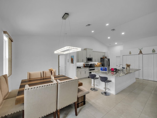 16430 71st Ln N, Loxahatchee, FL 33470 - kitchen featuring appliances with stainless steel finishes, a breakfast bar area, a kitchen island with sink, light stone counters, and high vaulted ceiling