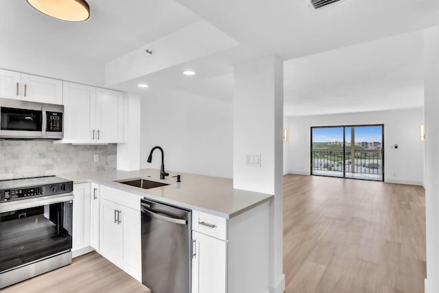 7076 Huntington Ln Unit 206, Delray Beach, FL 33446 - kitchen featuring appliances with stainless steel finishes, backsplash, light wood-type flooring, a peninsula, and open floor plan