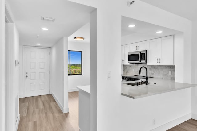 7076 Huntington Ln Unit 206, Delray Beach, FL 33446 - kitchen with stainless steel microwave, white cabinetry, light wood-type flooring, light countertops, and decorative backsplash