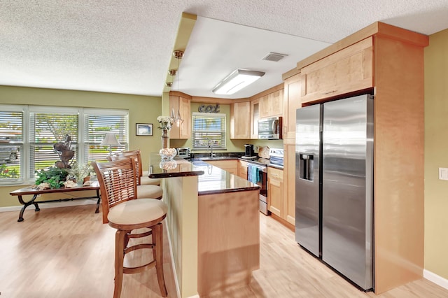 200 N High Point Blvd Unit C, Boynton Beach, FL 33435 - kitchen featuring stainless steel appliances, light brown cabinetry, a peninsula, light wood-type flooring, and a textured ceiling