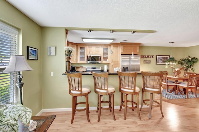 200 N High Point Blvd Unit C, Boynton Beach, FL 33435 - kitchen featuring appliances with stainless steel finishes, light wood-style flooring, a textured ceiling, glass insert cabinets, and a kitchen breakfast bar