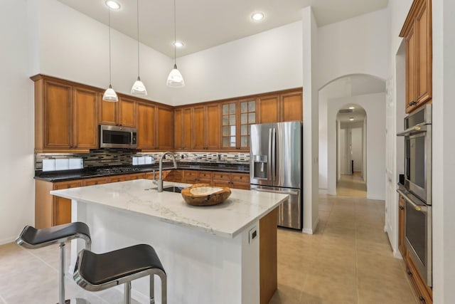 139 Sedona Way, Palm Beach Gardens, FL 33418 - kitchen featuring appliances with stainless steel finishes, a towering ceiling, brown cabinetry, arched walkways, and a sink
