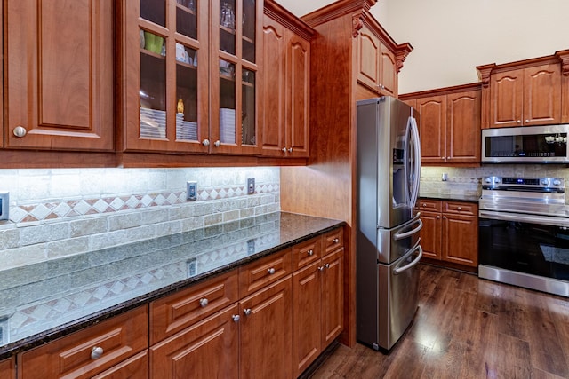 473 SW Dagget Ave, Port Saint Lucie, FL 34953 - kitchen featuring appliances with stainless steel finishes, backsplash, dark stone counters, glass insert cabinets, and dark wood-type flooring