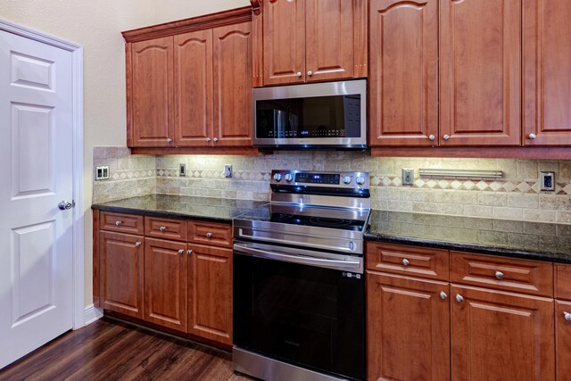473 SW Dagget Ave, Port Saint Lucie, FL 34953 - kitchen featuring stainless steel appliances, dark wood-style flooring, backsplash, dark stone countertops, and brown cabinets