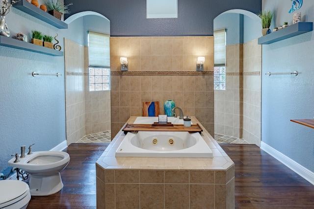 473 SW Dagget Ave, Port Saint Lucie, FL 34953 - bathroom featuring a textured wall, toilet, a tub with jets, wood finished floors, and a bidet