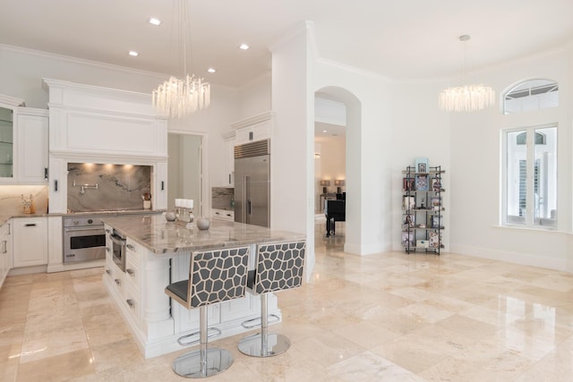 8246 Man O War Rd, Palm Beach Gardens, FL 33418 - kitchen with appliances with stainless steel finishes, a chandelier, arched walkways, light stone countertops, and ornamental molding