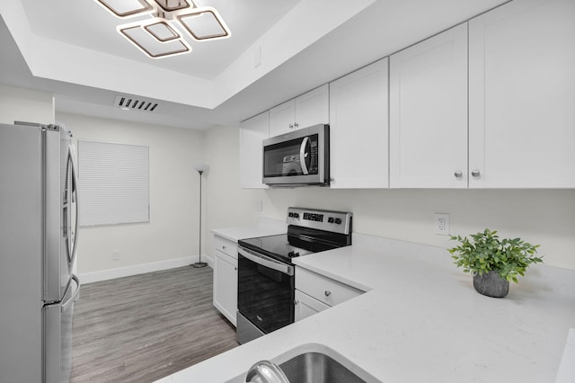 2517 S 17th St Unit 102, Fort Pierce, FL 34982 - kitchen featuring appliances with stainless steel finishes, light countertops, a tray ceiling, baseboards, and white cabinets