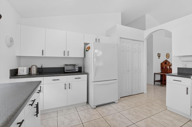 23440 Serene Meadow Dr S, Boca Raton, FL 33428 - kitchen featuring freestanding refrigerator, lofted ceiling, arched walkways, dark countertops, and white cabinetry