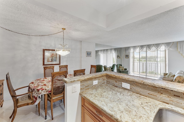 1009 N Ocean Blvd Unit 511, Pompano Beach, FL 33062 - kitchen with light tile patterned floors, a textured ceiling, a chandelier, light stone countertops, and backsplash