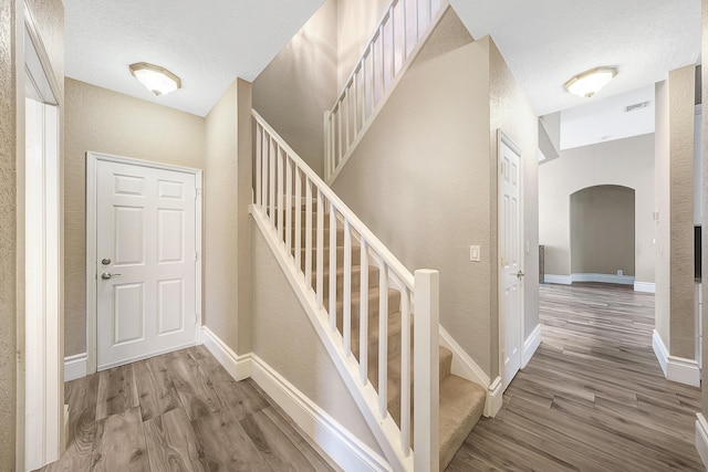 21480 Halstead Dr, Boca Raton, FL 33428 - foyer entrance with wood finished floors, a textured wall, arched walkways, a textured ceiling, and stairway