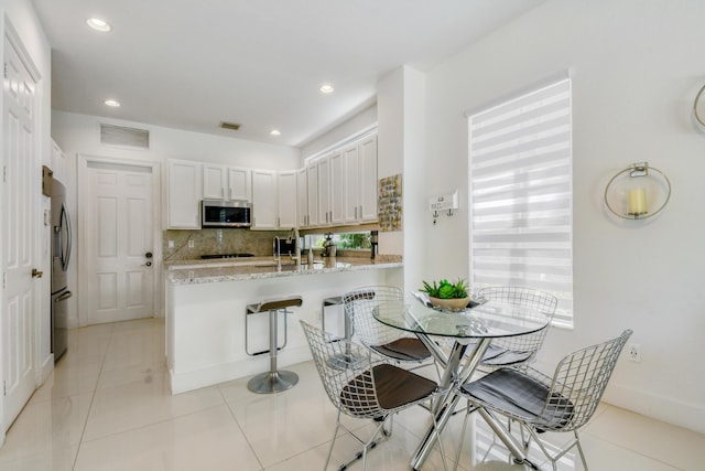 1522 Carafe Ct, Palm Beach Gardens, FL 33410 - kitchen featuring stainless steel appliances, a peninsula, decorative backsplash, light stone counters, and white cabinets